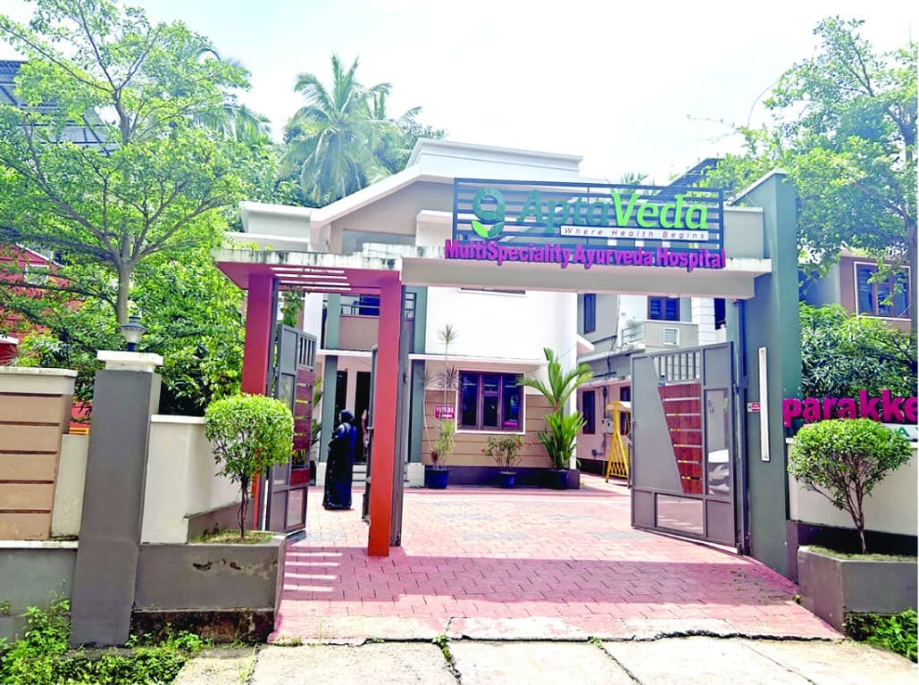 The entrance gate of Aptaveda Multispeciality Ayurveda Hospital, with the AptaVeda sign above a paved forecourt