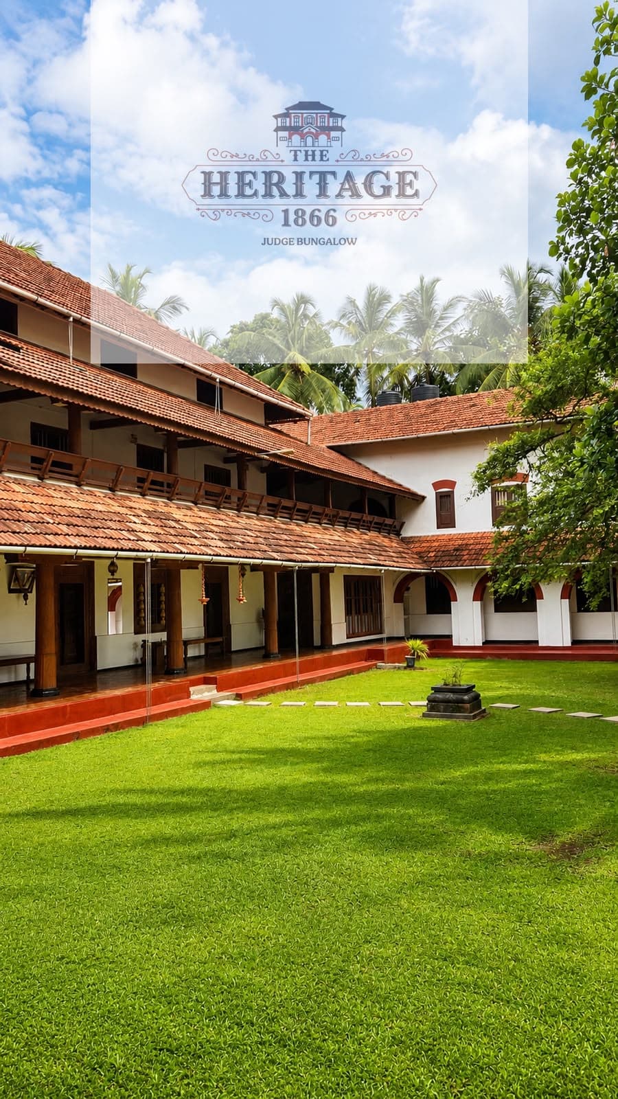 The lawn courtyard of The Heritage 1866 Judge Bungalow, with its tiled roofs, timber verandah and coconut palms