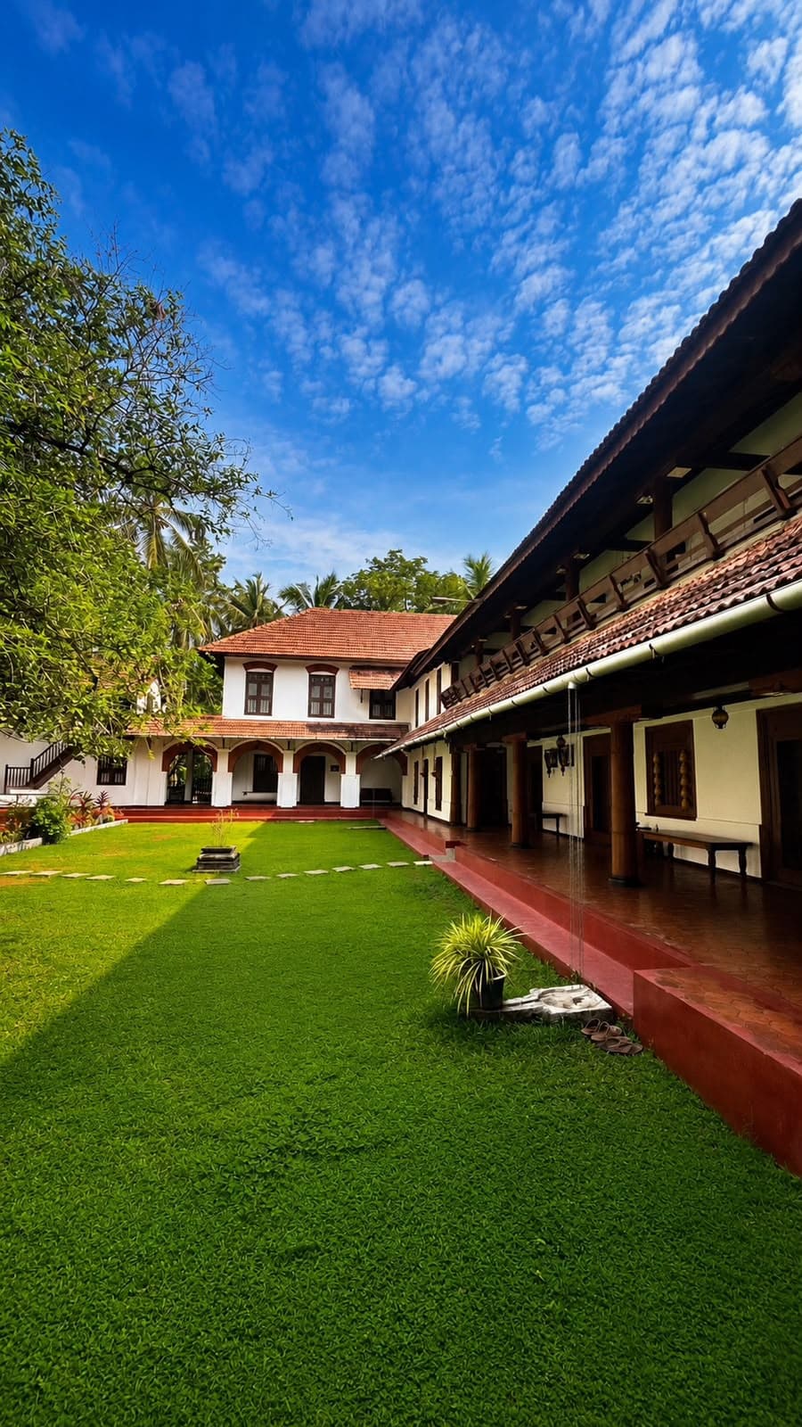 The lawn courtyard of The Heritage 1866, with its long tiled verandah, red oxide plinth and arched wing under a blue sky